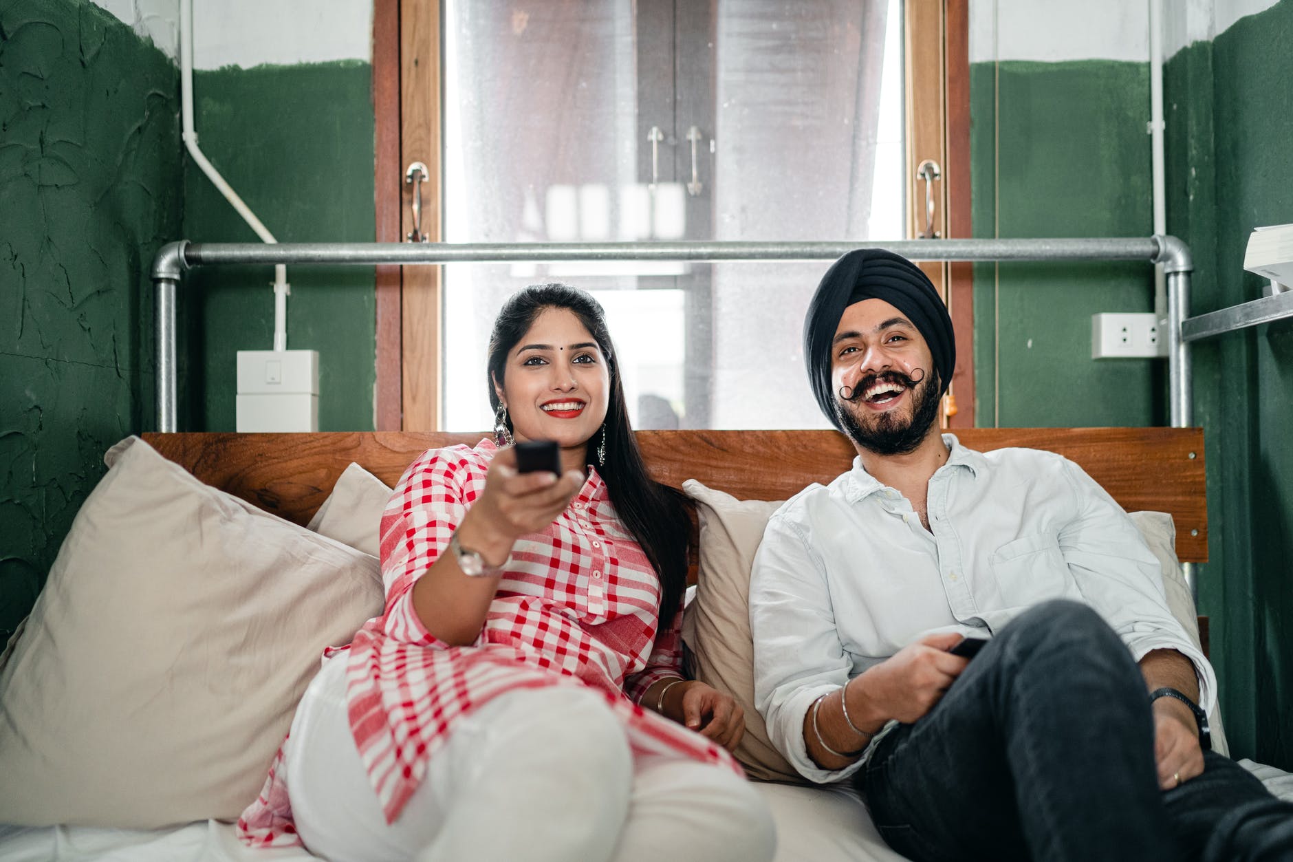 happy young indian couple watching tv in bedroom together